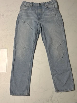 Ljusblå raka jeans från GANT - Snygga ljusblå jeans från GANT med klassisk femficksdesign och raka ben. Jeansen har en normal passform, knappstängning framtill och detaljerad GANT-logga på läderpatchen bak. Perfekta för dig som gillar stilrena och tidlösa jeans. Liten fläck på högra knäet och läderpatchen är sliten. Bra skick annars.