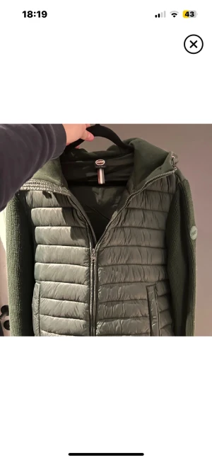 Grön pufferjacka Colmar Originals - Snygg grön pufferjacka från Colmar Originals med stickade ärmar och vadderad kropp. Jackan har huva, dragkedja framtill och Colmar-logga på ärmen. Perfekt för dig som gillar en sportig och chill stil. Flera fickor och cool quiltad design.