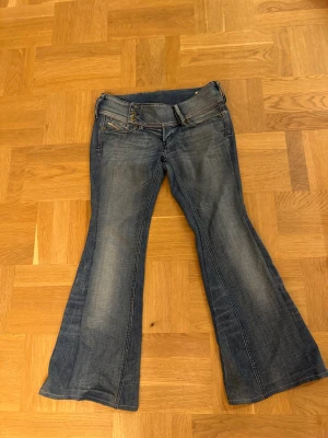 Disel jätte lågmidjade bootcut jeans - Snygga blå Diesel Cherock jeans med bootcut och låg midja. Klassisk femficksdesign, coola detaljer med flera knappar i guld och silver samt stretchmaterial för extra komfort. Perfekt passform och stilren tvätt med lätt slitning.