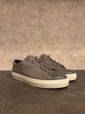 Axel Arigato Cap Toe - Säljer dessa Axel Arigato Cap Toe! Skorna har en stilren, rund tå och vit platt sula som ger en clean look. Perfekta för dig som gillar minimalistisk design och neutrala färger. 