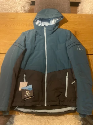 Blå och svart skidjacka från Salomon  - Snygg skidjacka från Salomon i storlek XL helt oanvänd. Perfekt för kalla dagar och skidåkning. 