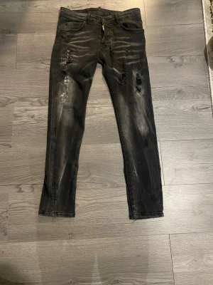 Svarta skinny jeans från Dsquared2 - Svarta jeans från Dsquared2 med slitna detaljer och skinny passform. Jeansen har klassisk femficksdesign, knappgylf och Dsquared2-logga vid linningen. Materialet är jeans med en lätt tvättad look och trasiga partier på framsidan för en edgy vibe.