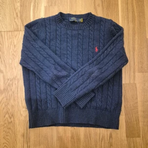 Marinblå stickad tröja Polo Ralph Lauren - Säljer en marinblå stickad tröja från Polo Ralph Lauren. Tröjan har kabelstickat mönster, rund hals och en röd broderad logga på bröstet. Långa ärmar och ribbade muddar ger en snygg och klassisk look. Perfekt för dig som gillar stilrena vibes. Det står M men den sitter mellan XS och S