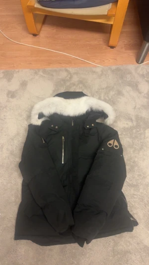 Svart dunjacka Moose Knuckles med päls - Säljer en svart dunjacka från Moose Knuckles med vit päls runt huvan och snygga metalldetaljer. Jackan har dragkedja framtill, långärmade ärmar och den ikoniska loggan på armen. Perfekt för kalla vinterdagar och riktigt stilren look. Storlek L/Xl passar båda!