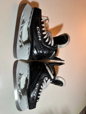 Svarta CCM skridskor strl 38 - Säljer ett par svarta CCM skridskor, modell AS550, med vita snören och grå/vita detaljer. Insidan är mjukt fodrad för extra komfort. Perfekt för dig som vill ha snygga och sportiga skridskor med stabil passform och cool design.