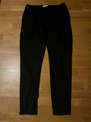 Svarta kostymbyxor Studio Total M - Snygga svarta kostymbyxor från Studio Total i storlek M. Klassisk rak passform med knapp och dragkedja framtill. Perfekta för en clean och stilren look, tillverkade i ett mjukt och bekvämt material.