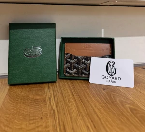 Korthållare  - Snygg plånbok från i brunt skinn och svart canvas med ikoniskt mönster. Kompakt och smidig design med flera kortfack, perfekt för dig som vill ha något stilrent och exklusivt i fickan. Levereras i original grön ask.