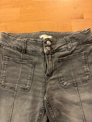 Grå bootcut jeans från Gina Tricot - Snygga grå jeans från Gina Tricot med bootcut passform och hög midja. Jeansen har två stora framfickor, dubbla knappar och dragkedja. Materialet är klassisk denim med en tvättad look som ger en cool vibe.