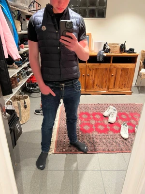 Svart dunväst från Moncler - Snygg svart dunväst från Moncler med hög krage och tryckknappar framtill. Västen har ett quiltat mönster och en tydlig Moncler-logga på bröstet. Perfekt för lager-på-lager och ger en stilren look.