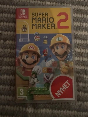 Super Mario Maker 2 till Nintendo Switch - Super Mario Maker 2 till Nintendo Switch där du kan skapa och spela egna Mario-banor. Omslaget är färgglatt med Mario och Luigi i byggarhjälmar. Perfekt för dig som gillar kreativitet och klassiska plattformsspel.