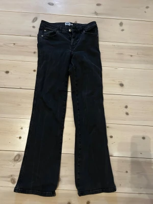 Svarta lågmidjade bootcut jeans med fickdetaljer - Snygga svarta/grå jeans med bootcut passform och klassiska fem fickor . Baksidan har fickor med lock och knappdetaljer. Jeansen har normal midja och är tillverkade i ett mjukt bomullsmaterial med lite stretch för extra komfort. Ngt långa för mig som är 164 cm, finns nån skavank nere vid hälen.