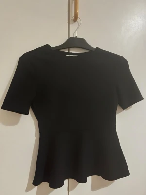 Svart topp - Snygg svart topp från hm i storlek xs med korta ärmar och rund halsringning. Modellen har en markerad midja och utsvängd nederdel har endast använt någon få gång så är jättebra skick🤍