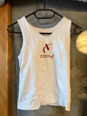 Vit linnetopp från Coola Sweden - Säljer en vit linnetopp från Coola Sweden med broderad röd logga och text på bröstet. Toppen har en ärmlös design och mjuk bomullskänsla, perfekt för en avslappnad och sportig stil. Passar dig som gillar enkel men snygg look.