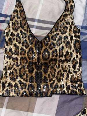 Leopardmönstrad paljettopp - Snygg leopardmönstrad topp o byxor med paljetter och djup v-ringning. Perfekt för dig som vill sticka ut och addera lite extra bling till outfiten. Toppen är ärmlös och har en croppad passform. 
