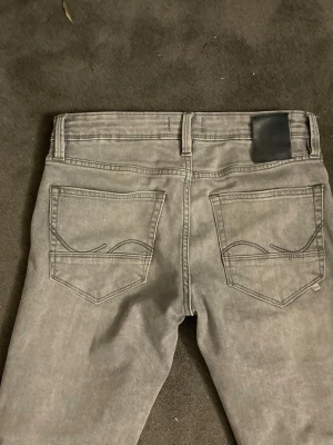 Grå slim jeans med raka ben - Snygga grå jeans med raka ben. Jeansen har diskreta sömmar på bakfickorna och en svart patch vid linningen. Perfekta för dig som gillar en clean och stilren look.