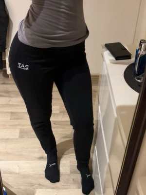 EA7 Armani mjukisbyxor  - Svarta mjukisbyxor från EA7 med vit logga på vänster lår. Byxorna har en slim passform och är tillverkade i mjukt material som känns skönt mot huden. Perfekta för en avslappnad och sportig stil.