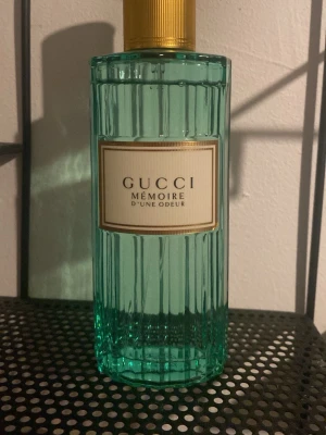 Gucci Mémoire d'une Odeur parfym - Gucci Mémoire d'une Odeur parfym i en elegant, räfflad glasflaska med ljusgrön färg och guldfärgat lock. Flaskan har en klassisk etikett med svart text och ger en lyxig känsla. Perfekt för dig som gillar exklusiva dofter och snygg design.