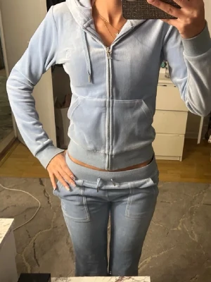 Ljusblå juicy couture byxor - Säljer ett par ljusblå mjukisbyxor med snörning i midjan och fickor både fram och bak. OBS! Säljer endast byxorna och inte hela settet. Finns små ”hål” där bak och ngr få vid insidan benen, men syns inte. Byxorna har ett pytte litet håll längst ner vid ena benet men det är inget som syns. 