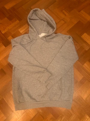 Grå hoodie med huva och ficka - Klassisk grå hoodie med huva och dragsko samt en stor magficka framtill. Hoodien har långa ärmar och ribbade muddar vid ärmslut och nederkant. Perfekt för en chill och avslappnad stil. Storlek S men skulle själv säga att det är M! Skriv vid funderingar! 