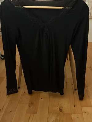 Intimissimi tröja  - Svart långärmad tröja från intimissimi med v-ringning och fina spetsdetaljer vid halsringningen och ärmsluten. Tunn och stretchig, perfekt att styla med jeans eller kjol. Enkel men ändå elegant look.