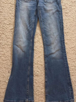 Blå bootcut jeans storlek 152 - Säljer ett par blå bootcut jeans med snygga slitningar och klassisk femficksdesign. Jeansen har en lätt utsvängd passform nedtill och är  tillverkade i ett mjukt denimtyg som ger en avslappnad look. Perfekta för dig som gillar stockholmsstilen och vill ha ett par jeans som sticker ut.