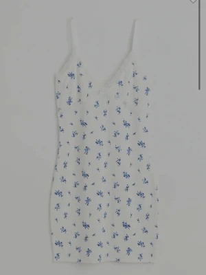 Vit blommig klänning spets - Supersöt vit klänning med blå blommigt mönster och tunna axelband. V-ringad med spetsdetaljer upptill och ribbad struktur i tyget. Perfekt till studenten eller skolavslutningen. Endast använd en gång🥰🌸