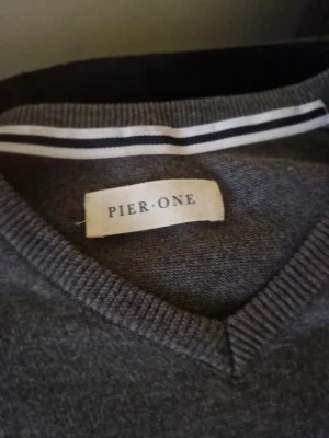 Grå v-ringad tröja från Pier One - En enkel och snygg grå tröja från Pier One med v-ringad hals och långa ärmar. Tröjan har ribbade muddar vid ärmslut och nederkant. Materialet ser ut att vara mjukt och tunt, perfekt för lager-på-lager. Passar till många olika stilar.