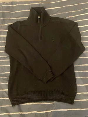 Svart stickad halvzip-tröja - Snygg svart stickad tröja med halv dragkedja och hög krage. Liten broderad logga på bröstet. Tröjan har ribbade muddar vid ärmslut och nederkant, perfekt för en clean och stilren look. Märke: boomerang, ett svenskt exklusivt märke. Vet inte vad den kosta nu pris men priset kan sänkas vid snabb affär!