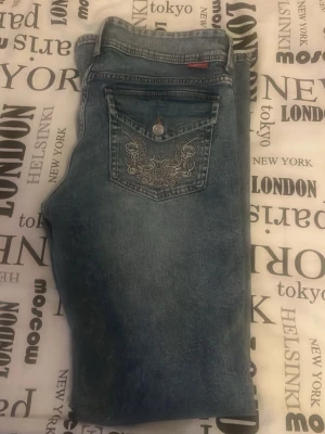 Blå bootcut h&m jeans med mönster på backfickan, kan passa 38  - Snygga blå bootcut jeans med ljus tvätt och broderad bakficka. Jeansen har klassisk femficksdesign och en knapp framtill. Perfekta för dig som gillar en avslappnad men trendig look.