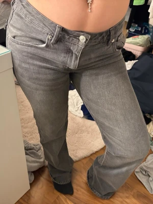 Gråa bootcut jeans med låg midja - Snygga gråa jeans med bootcut-modell och låg midja. Jeansen har klassisk femficksdesign och stängs med knapp och dragkedja. Perfekta för dig som gillar en avslappnad och trendig look.