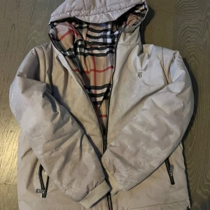 burberry jacka - Säljer en snygg pufferjacka från Burberry med klassiskt rutig mönster i beige, svart, vit och röd. Passar dig från 175 till 183cm. Riktigt fet o skön till vintern