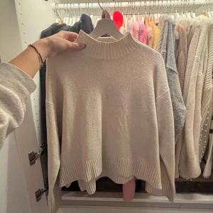 Beige stickad polotröja - Säljer en beige stickad polotröja med ribbad hög krage och ribbade muddar. Tröjan har en loose passform och är perfekt för att hålla sig varm under kyliga dagar. Enkel och stilren design som funkar till många olika outfits och den kommer ursprungligen från uniqlo! 🍓 hör av er om eventuella frågor!