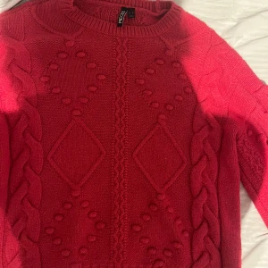 Rosa stickad tröja från Pieces - Säljer en rosa stickad tröja från Pieces med grova flätor längs ärmarna och snygga mönster med bollar och rutor på framsidan. Rund hals och långärmad modell, perfekt för kyliga dagar. Supermysig och trendig färg!