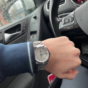 Gant klocka - Säljer en stilren klocka från GANT med rund vit urtavla och datumvisning. Klockan har ett klassiskt armband i blankt silverfärgat metall och tydliga indexmarkeringar. Kommer med originalask och certifikat. Perfekt för dig som gillar clean design. Nypris 2400