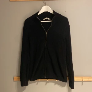 Svart ribbad kofta från H&M - Svart ribbad kofta från H&M med hel dragkedja framtill och långärmad design. Tröjan har en enkel och clean look med ståkrage och är gjord i ett stickat material som känns mjukt och skönt. Perfekt för dig som gillar minimalistisk stil.