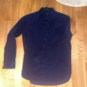 Manchester skjorta/overshirt - Säljer en mörkblå manchesterskjorta från Uniqlo i storlek S. Skjortan har klassisk krage, långa ärmar och knäppning framtill. Perfekt för dig som gillar en stilren och enkel look.
