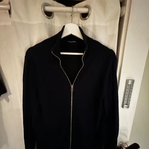 Svart kofta med dragkedja från Jack & Jones - Stilren svart kofta från Jack & Jones med hel dragkedja framtill och hög krage. Perfekt för lager-på-lager och enkel att matcha med andra plagg. Långärmad och i mjukt material som känns skönt mot huden.