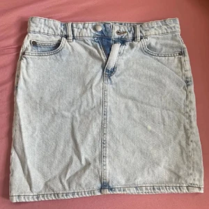 Ljusblå jeanskjol från Lindex - Säljer en ljusblå jeanskjol från Lindex i klassisk femficksmodell med bälteshällor och knappstängning fram. Kjolen är kort och har raka linjer, perfekt till sneakers eller boots. Materialet är bomull och den har en normal passform. Använd 2 gånger