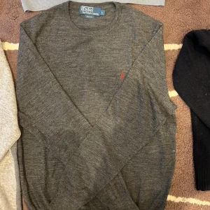 Mörkgrå stickad tröja Polo Ralph Lauren L - Mörkgrå långärmad tröja från Polo Ralph Lauren i slim fit-modell. Tröjan har rund halsringning och en liten broderad logga i rött på bröstet. Tillverkad i mjuk ull, perfekt för kyliga dagar. Lappen i nacken sitte löst på ena sidan men absolut ingenting som stör utseendet på tröjan. Står stl L men är mycket mer av en stl M!🙌