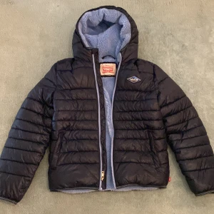 Blå pufferjacka från Levi's 14A - Säljer en blå pufferjacka från Levi's Expeditionaries med ljusblå teddyfoder och huva. Jackan har dragkedja framtill och ett snyggt Levi's-märke på bröstet. Perfekt för kalla dagar och har en cool, sportig vibe. Passar dig som gillar streetwear och vill hålla dig varm.