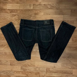 Svarta jeans från EastWest - Snygga svarta jeans från EastWest med klassisk femficksdesign och raka ben. Jeansen har mörk tvätt, subtila sömmar och en patch med logga bak i midjan. Perfekta för dig som gillar stilrena och tidlösa jeans med normal passform.