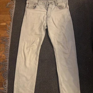 Levi's 501 ljusa jeans med raka ben - Snygga ljusa Levi's 501 jeans med klassisk femficksdesign och raka ben. Jeansen har tydliga svarta sömmar, knappgylf och den ikoniska läderlappen bak i midjan. Perfekt för dig som gillar tidlös stil och vill sticka ut med en ljus tvätt finns ett hål på baksidan.