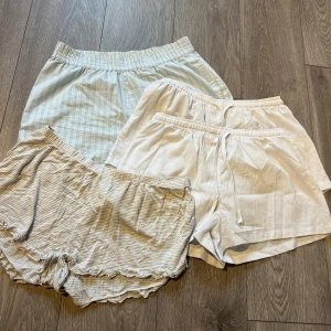 4-pack shorts från Bik Bok & H&M - Säljer tre par mjuka och sköna shorts i ljusa färger. Ett par från Bik Bok i ljusblått med vita ränder, två par från H&M i beige och vitt med tunna ränder. Alla har elastisk midja, ett par har snörning och ett par har volangkant. Perfekta för chill dagar hemma.