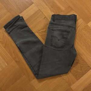 Levi's 512 slim taper mörk grå jeans strl. 14A/164cm - Säljer ett par svarta Levi's 512 jeans i slim fit. Jeansen har klassisk femficksdesign, dragkedjegylf och smal passform hela vägen ner. Snyggt tvättade med en mörkgrå ton och diskreta slitningar. Åtstramningsbara i midjan. 