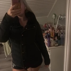 Svart pufferjacka med dragkedja - Säljer en svart pufferjacka med hög krage och dragkedja samt knappar framtill. Jackan har långa ärmar och två snedställda fickor med dragkedja. Perfekt för kyliga dagar och har en snygg, figurnära passform.