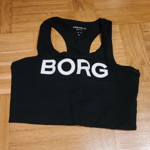 Svart linnetopp från Björn Borg - Svart linnetopp från Björn Borg med stor vit logga framtill. Sportig modell med brottarrygg och croppad passform, perfekt för träning. Tillverkad i mjukt och stretchigt material som ger bra rörelsefrihet.