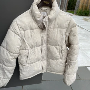 Beige pufferjacka från Gina Tricot young - Säljer en beige pufferjacka från Gina Tricot med hög krage och dragkedja framtill. Jackan har två fickor på sidorna och quiltad design som ger en riktigt snygg och trendig look. Perfekt för kyliga dagar när du vill vara både varm och stilren.
