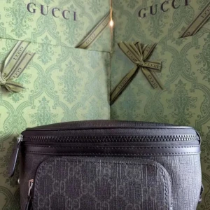 Svart magväska i skinn - Snygg svart axelväska från i i präglat skinn med diskret mönster. Väskan har justerbar rem, dragkedja upptill och ett praktiskt ytterfack. Perfekt för dig som vill ha en stilren och lyxig accessoar med ikonisk logga.