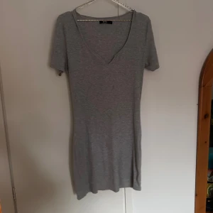 Grå ribbad kortklänning från BikBok - En enkel och stilren grå kortklänning från BikBok i ribbat material. Klänningen har v-ringning och korta ärmar. Använd men i bra skick 