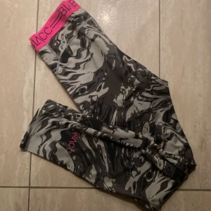 BLACC leggings med marmorprint - Snygga leggings från BLACC med svart och grått marmorprint och bred, rosa resår i midjan med logga. Tillverkade i stretchigt material av polyester och elastan, perfekta för träning eller chill. Superskön passform och cool design.